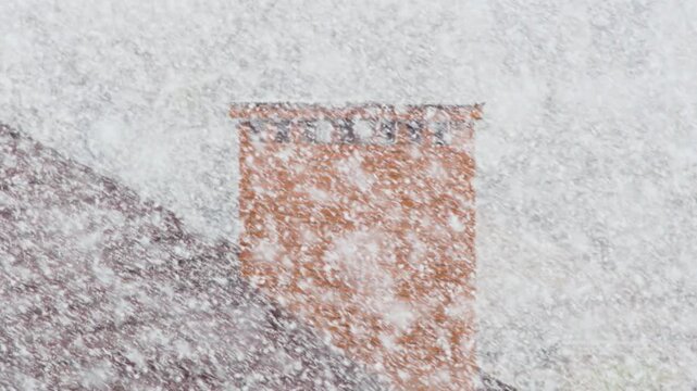 Unseasonal heavy snowfall in April highlights the increasing unpredictability of weather patterns and the impact of climate change. Snowstorm above the roof of a house with a chimney
