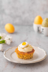 Lemon Poppy Seed Cupcakes with lemon curd and cream cheese topping and Fried Egg candies. Colourful Easter eggs, flowers on a stone background, top view. Easter holiday and festive food.