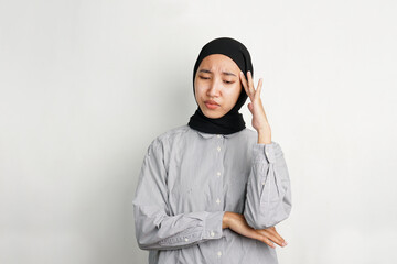 Young Asian woman touching her temple with a pained expression, indicating dizziness or headache,...