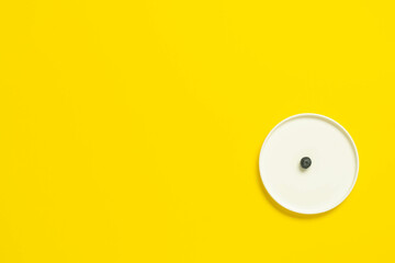 Minimalist white plate with tiny black seed on yellow background.