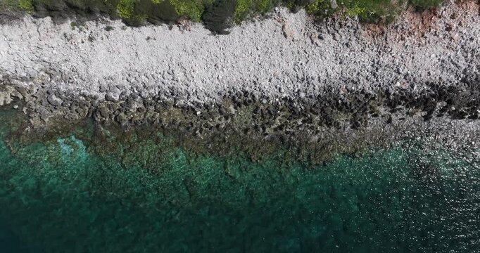 Birdseye aerial track of clear blue water and white stone beach near Limeni, Greece in the Peloponeese Mani Peninsula.