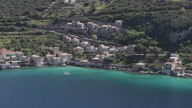 Aerial pan along homes on green mountain side in Limeni, Greece in the Peloponeese region.