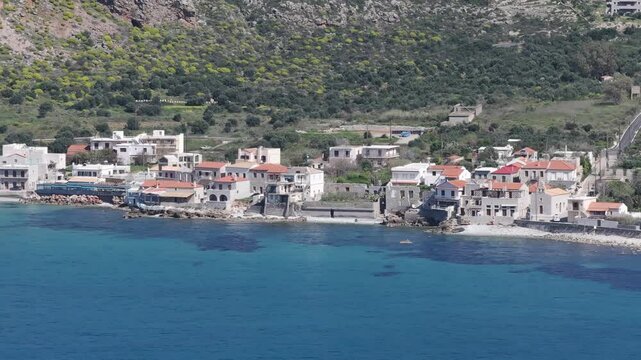 Aerial pan along houses on the front of coastal village Limeni, Greece with blue water and surrounding mountains in the Peloponeese.