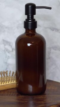Amber glass shampoo bottle with bamboo hairbrush on dark wooden board and marble background. Minimalist natural, eco-friendly haircare and sustainable beauty product styling.