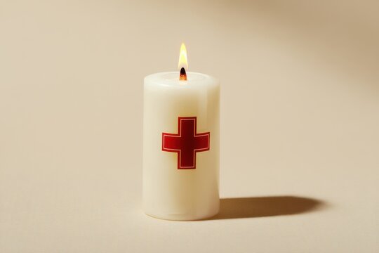 
White church candle with a red cross symbol, isolated on a beige background