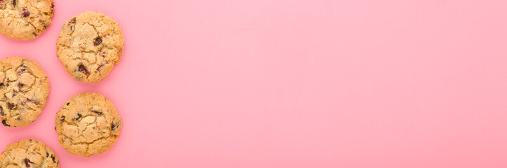 Dry cookies with chocolate pieces on light pink table background. Pastel color. Closeup. Sweet snack. Wide banner. Empty place for text. Top down view.
