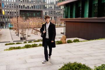 A young, confident Caucasian man aged 25, dressed in a black coat and a white headset on his ears,...