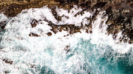 Drone point of view of Atlantic ocean waves meet with underwater pointed rocky. Blue rough sea with big waves with foam crashing against the rocks, south of Tenerife, Canary island