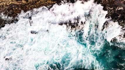 Drone point of view of Atlantic ocean waves meet with underwater pointed rocky. Blue rough sea with big waves with foam crashing against the rocks, south of Tenerife, Canary island