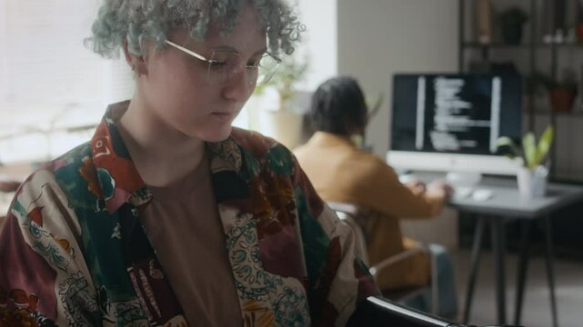 Tilt up shot of casually dressed gen Z woman with bionic hand standing near printer in office and reading document