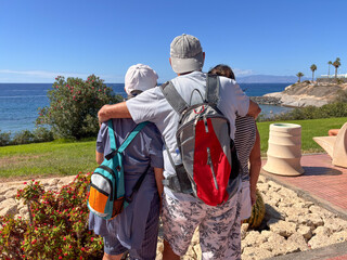 Rear view of three seniors people embracing outdoors face the ocean admiring the seascape enjoying Vacation and Freedom in a sunny day. Happy Retirement Lifestyle Concept