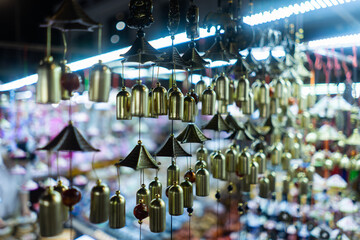 Wind chimes hang on Asian market stall glowing with lights creating cultural charm, Decorative bells display on night marketplace radiates exotic beauty