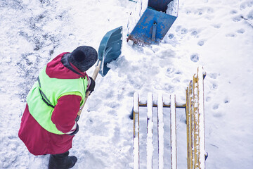 Snow falls from a shovel as a janitor diligently clears the pedestrian area of a street in a snowy...
