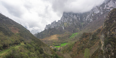 Mountain landscape on a cloudy day with green meadows in the valley and enormous mountain peaks covered with clouds