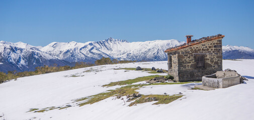 Mountain hut in the foreground surrounded with snow and mountain peaks in the background