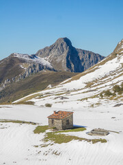 Mountain hut in the foreground surrounded with snow and a mountain peak in the background
