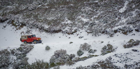 Red 4 wheel drive climbing a mountain trail completely covered with snow