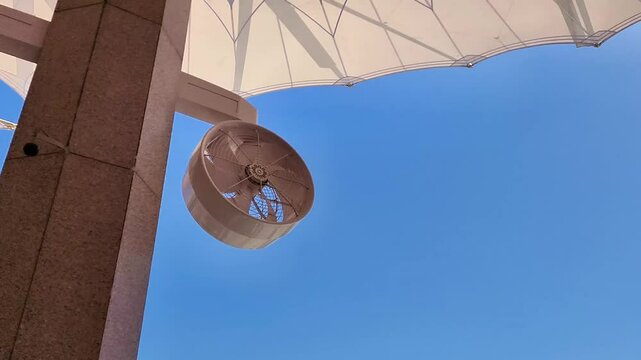 A fan under the umbrella of the Prophets Mosque with a bright blue sky background in a hot but cool weather atmosphere