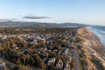 Aerial drone picture of Manzanita Beach on the Oregon Coast, showing waves of the Pacific Ocean, small coastal town, sunset, sandy shoreline, forested mountains. Perfect for travel and tourism themes © Hrach