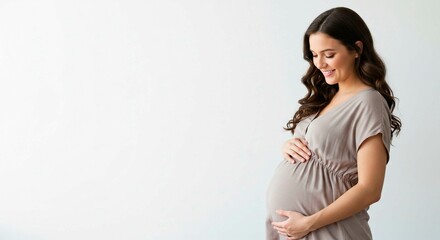 Radiant expectant mother with gentle smile embraces her belly, embodying the joy and anticipation of new life, wearing neutral-colored dress.