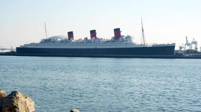 Long Beach, California - January 11, 2025: Iconic RMS Queen Mary moored in Long Beach, California, showcasing its majestic silhouette and reflecting off the tranquil waters.