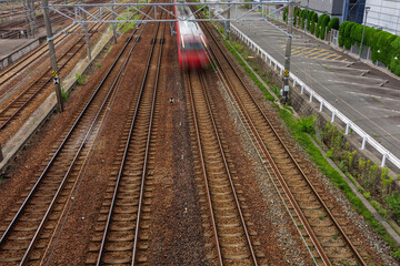 Fototapeta premium Blurred motion of rush hour commuter traveling on multiple railway tracks during the day in an urban environment, showcasing transportation and speed surrounded by greenery and infrastructure.
