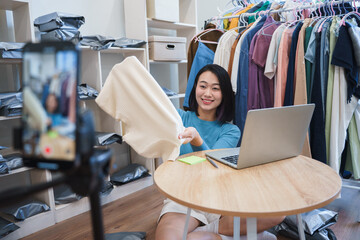 Young woman showcasing clothing in an organized room filled with garments and packages during an...