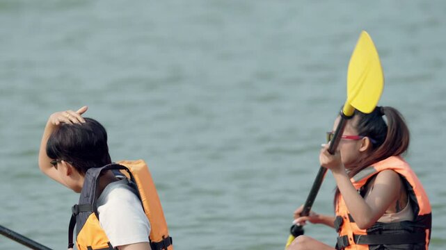A woman in a life jacket is sitting in a kayak. She is holding a paddle. There are two other people in the background