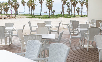 Empty outdoor terrace of the restaurant cafe by the sandy beach with palm trees. Vacation and summer