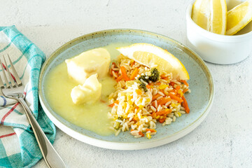 Cod fish steak in lemon sauce and vegetable rice dish, napkin, fork, on white marble stone table, copy space, light and airy