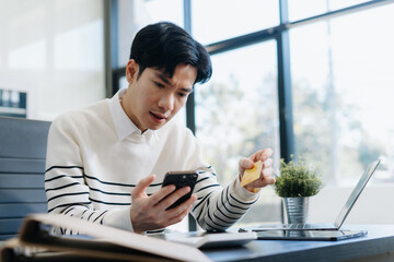 Serious young man sit at workplace desk in office use calculator calculates monthly expenses,...