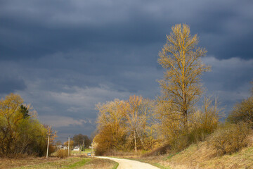 Dramatic cloudy sky before a thunderstorm over a peaceful Ukrainian village. Storm clouds, green grass, bare trees in early spring. Stormy sky over village