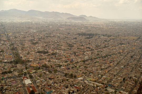 Aerial view of a sprawling cityscape with mountains in the background under a cloudy sky. Mexico City, Mexico