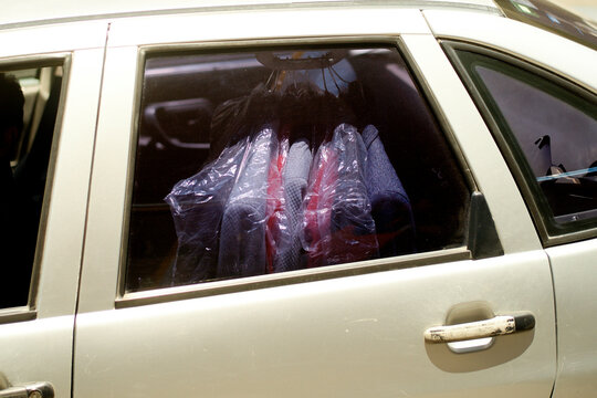 Garments and suits covered with plastic hanging inside a car seen through the window. Mexico City, Mexico