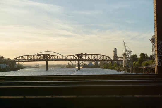 Industrial bridge spanning a river at sunset with a crane in the background. Oregon, USA