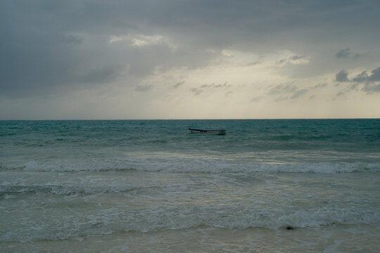 Stormy sky over a distant boat on the open ocean with gentle waves reaching the shore. Tanzania, Zanzibar