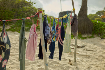 Colorful clothes hang on a rustic clothesline on a sandy beach with lush greenery and trees. Dar es Salaam, Tanzania