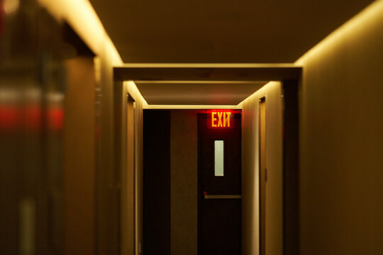 Dimly lit hallway with illuminated exit sign and closed doors. New York City, NY, USA