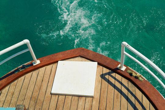 Boat prow over turquoise ocean water with wooden deck and white railings. Mykonos, Greece