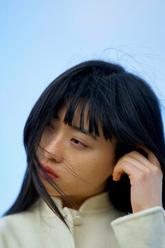 Woman with long hair touches her face thoughtfully against a blue sky background. Brandenburg, Germany