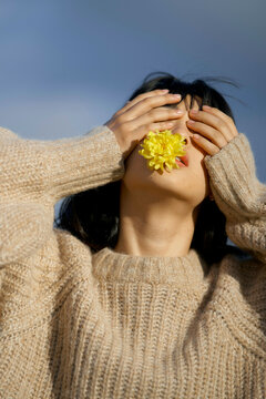 Woman in a beige sweater holds a yellow flower over her mouth, with sky in the background. Brandenburg, Germany
