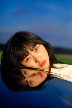Woman with black hair reflected on a shiny surface against a blue sky background. Brandenburg, Germany