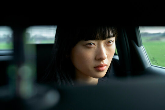 Young woman with straight black hair intensely gazing through a car rear window. Brandenburg, Germany