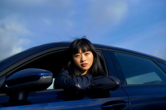 Woman leaning out of a car window under a blue sky, looking thoughtfully into the distance. Brandenburg, Germany