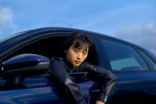 Woman leans out of a car window with a calm expression under a clear blue sky. Brandenburg, Germany
