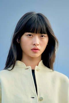 Woman with long dark hair wearing a beige coat against a blue background. Brandenburg, Germany