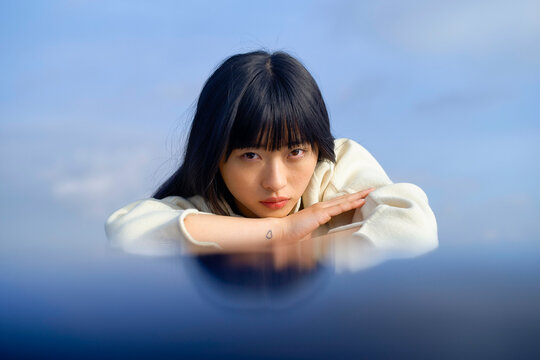 Woman with long hair resting her head on arms, gazing with a serene expression outdoors. Brandenburg, Germany