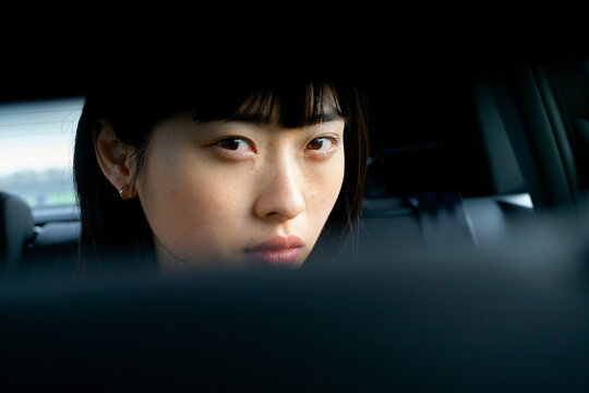 Woman with bangs looking intently through rearview mirror in a dimly lit car interior. Brandenburg, Germany