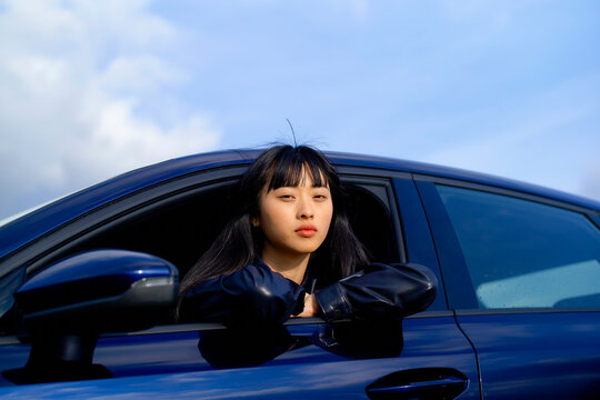 Young woman with long hair leans out of a car window against a blue sky backdrop. Brandenburg, Germany