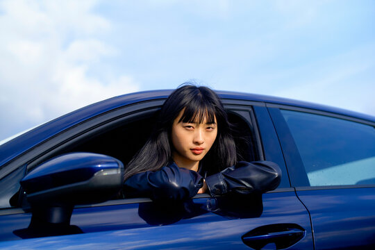 Woman with black hair leans out car window under a clear blue sky. Brandenburg, Germany